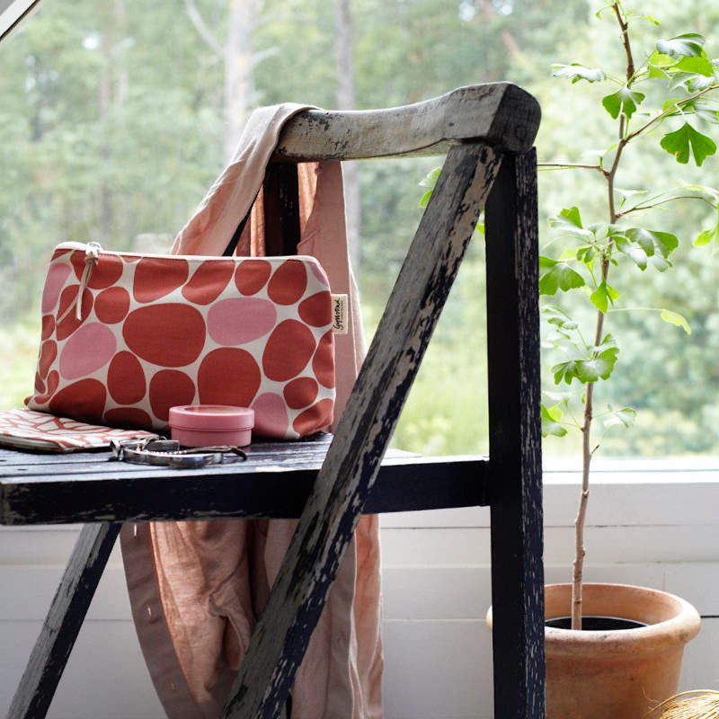 Gyllstad Studio. Kosmetiktasche aus Bio-Baumwolle. Rosa & terracotta. Tasche auf einem Stuhl vor einem Fenster.