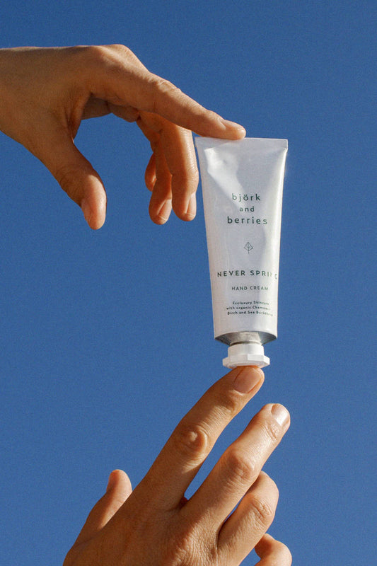 Björk & Berries Never Spring hand cream, hands holding a tube + blue sky